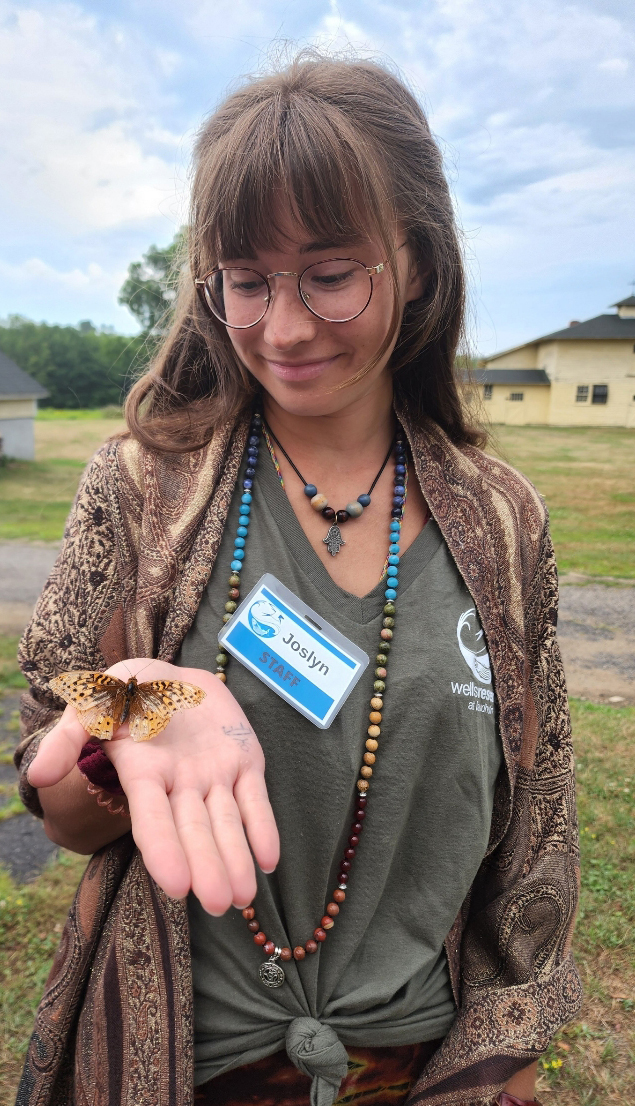 Joslyn, 2022 summer camp assistant, holds a butterfly in the palm of her hand.