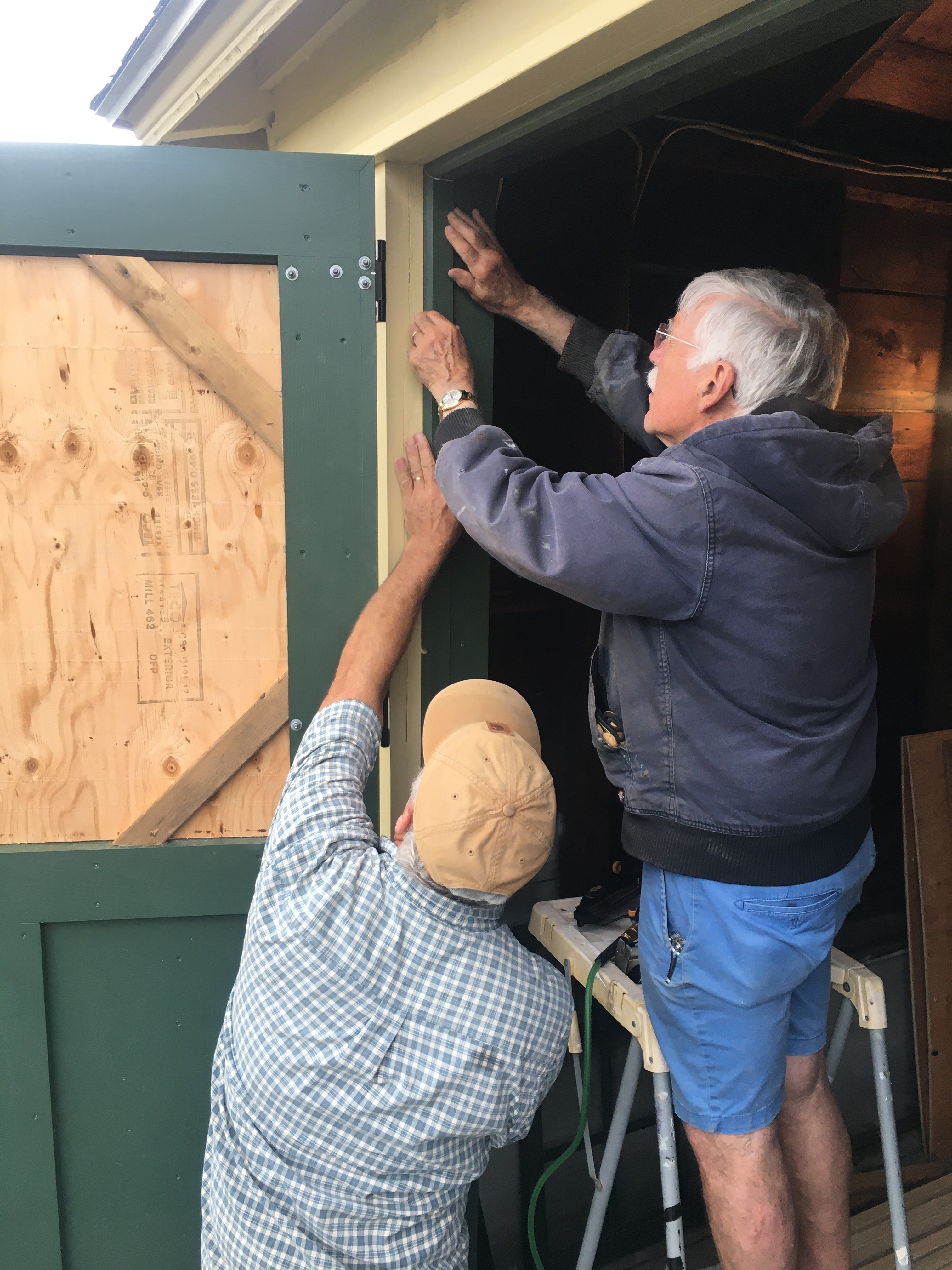 Volunteer Peter Anthony (on ladder) assists facilities director brian greenwood with precise and accurate positioning of a trim board after the first replacement door was hung on the five-bay garage.