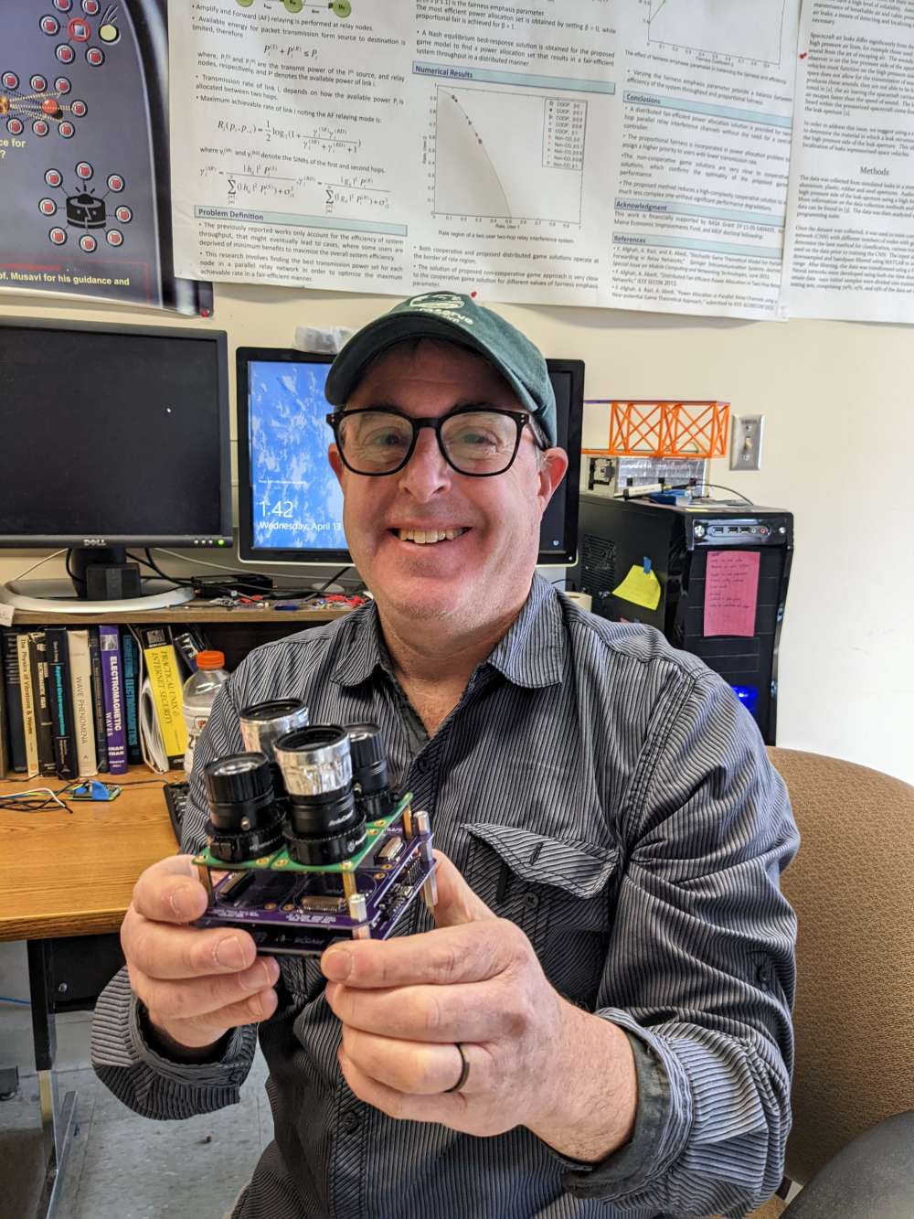 Dr. Jason Goldstein shows off a test model of the MESAT1 imaging module. Its four lenses are fitted with filters designed to capture images from specific portions of the color spectrum required by three student experiments carried by the satellite. Photo: Rebecca Kibler.