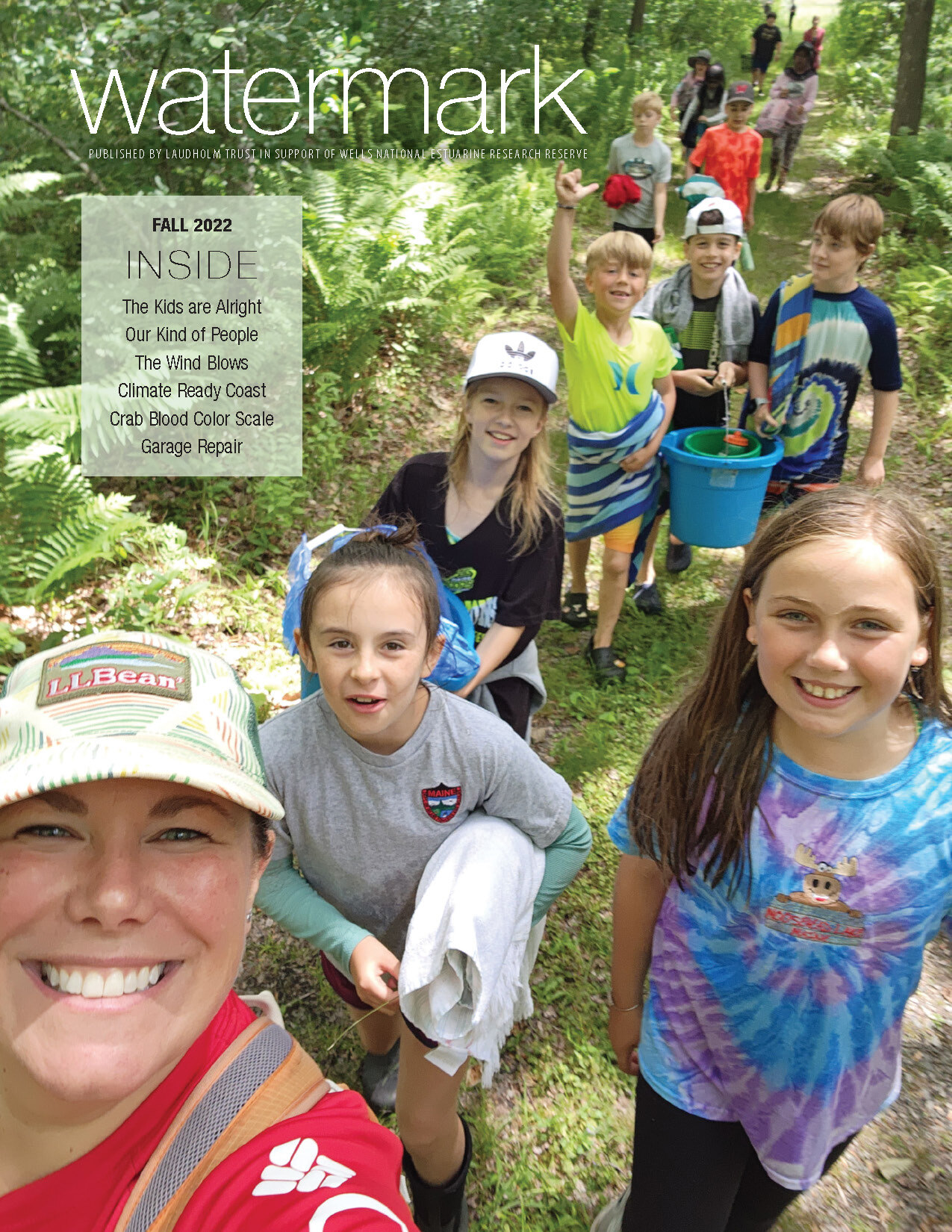 Cover of the fall 2022 Watermark newsletter showing the camp coordinator and a line of children walking on a trail through the woods during summer 2022.